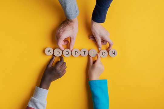 adoption adoptee therapy hands putting letter tiles together to spell adoption on a yellow background 